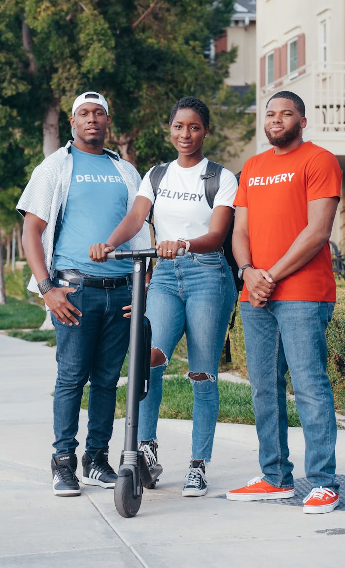 Three delivery team members standing with an electric scooter outdoors, smiling.