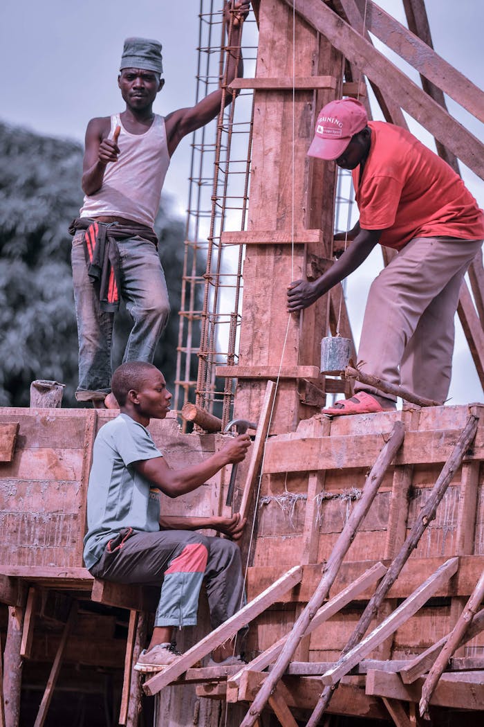 Three construction workers collaborate on a wooden structure under a clear sky.