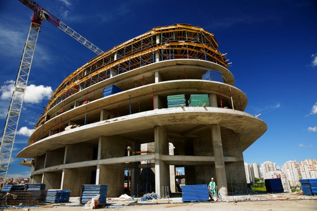 unfinished-gray-concrete-building-1463917 Low angle view of a circular building under construction with a crane, clear blue sky.
